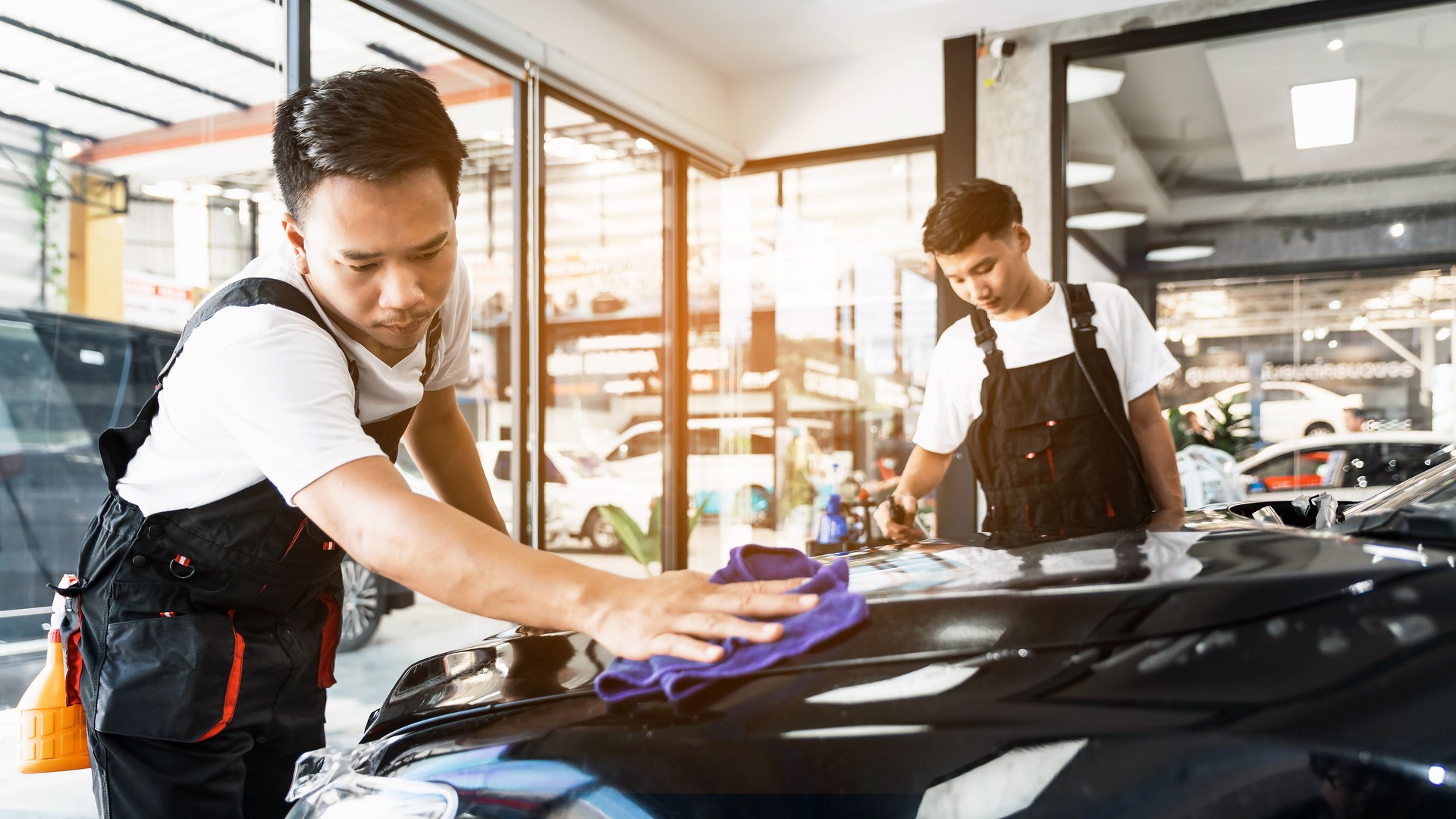 Men cleaning the car and remove a scratch with a dry blue microfiber towel in front hood, car detailing (or valeting) concept. Automobile professional cleaning service.